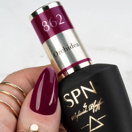 Hand holding SPN Nails UV/LED Gel Polish 862 Orchidea bottle, showcasing its rich red-purple shade on manicured nails.