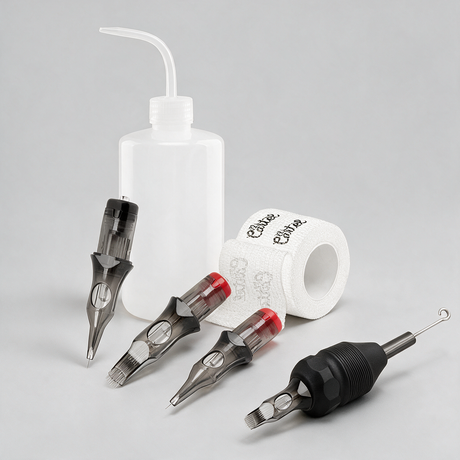 Tattoo machine needle cartridges and accessories arranged on a light gray studio background, including three needle cartridges with black and red tips, a black handpiece, a white plastic wash bottle with a curved tube, and a roll of branded tattoo tape.