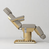 Manufakturo Aurélie beauty bed in Pearl Greige with gold-finished base, side view with backrest raised and leg section lowered.