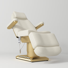 Manufakturo Aurélie beauty bed in Creamy with gold-finished base, reclined front three-quarter view.