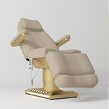 Manufakturo Aurélie beauty bed in Warm Beige with gold-finished base, reclined front three-quarter view.