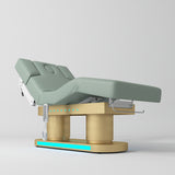 An adjustable medical examination table with a pale sage green padded surface and a gold-colored metal support frame, shown on a light gray studio background.