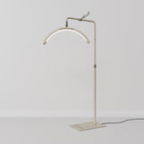A modern floor lamp with an adjustable metal stand, a curved light bar, and a black power cord, shown against a neutral light gray background.