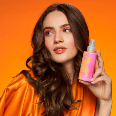 Model holding OnlyBio Hair Cycling Nutrition Kit serum bottle with vibrant orange background. Vegan hair care product for healthy and nourished hair, available at Roxie Cosmetics.