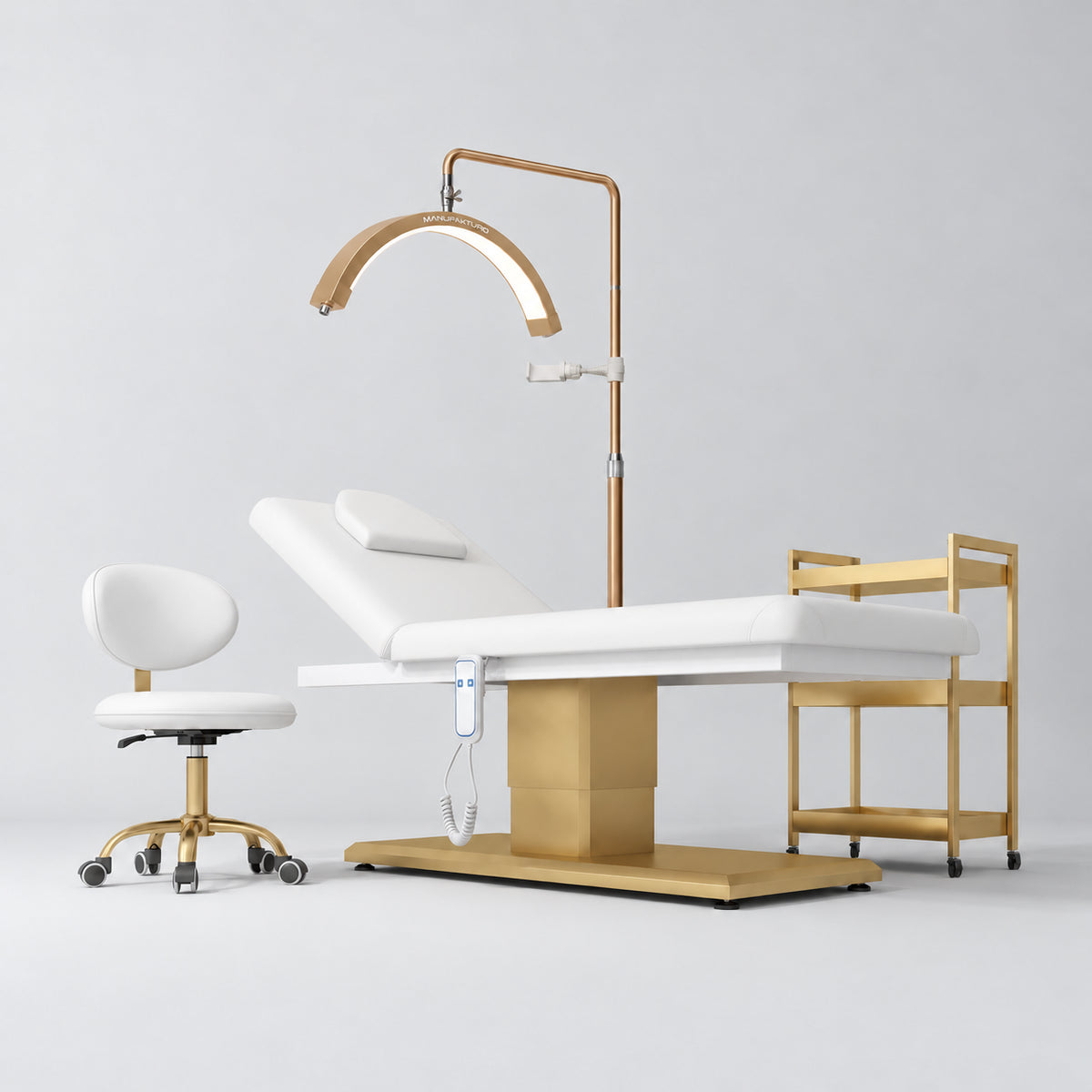 Manufakturo Chérie White four-piece salon set with electric massage bed, matching rolling beauty chair, V3 Pro Gold treatment lamp and empty three-tier gold trolley.
