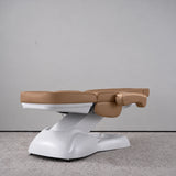 Manufakturo Grace Caramel electric beauty bed lying flat, with wooden armrest caps and the original white inclined lift and sculpted base.