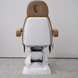 Rear view of the Manufakturo Grace Caramel electric beauty bed, showing the upholstered headrest, white rigid rear cover and adjustment mechanism.
