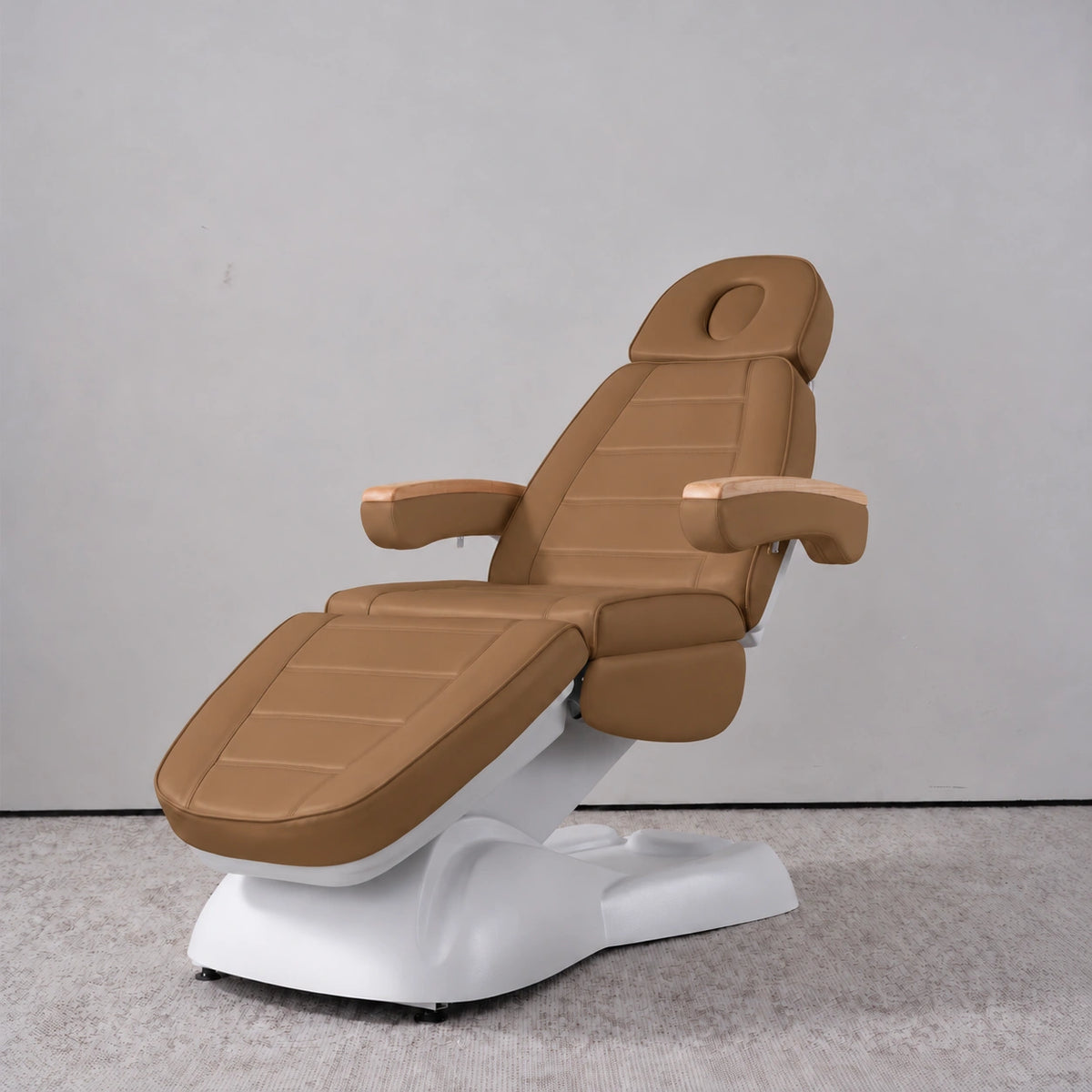 Manufakturo Grace Caramel electric beauty bed in a treatment position, with wooden armrest caps and a white sculpted base.