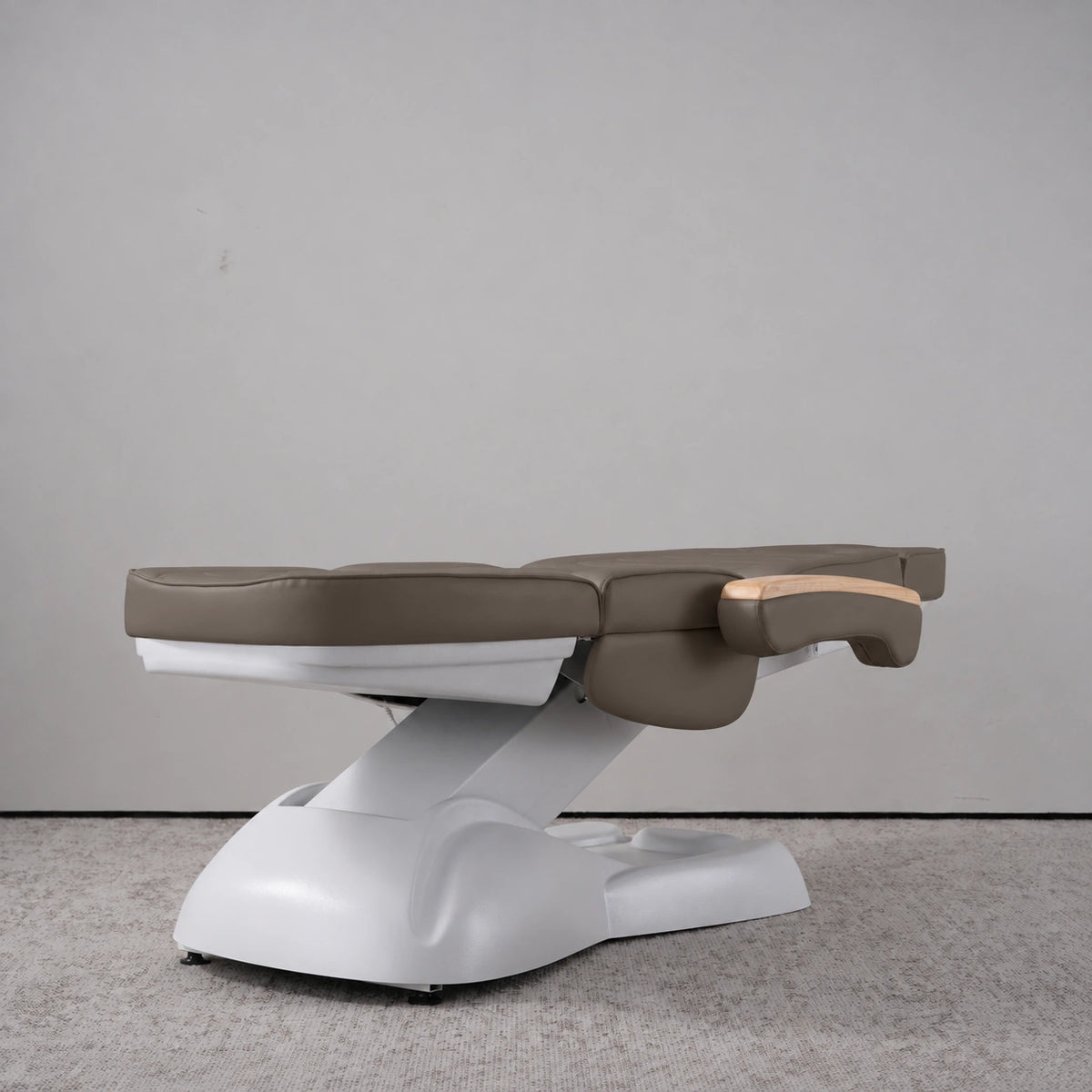 Manufakturo Grace Cocoa Mocha electric beauty bed lying flat, with wooden armrest caps and the original white inclined lift and sculpted base.