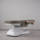Manufakturo Grace Cocoa Mocha electric beauty bed lying flat, with wooden armrest caps and the original white inclined lift and sculpted base.