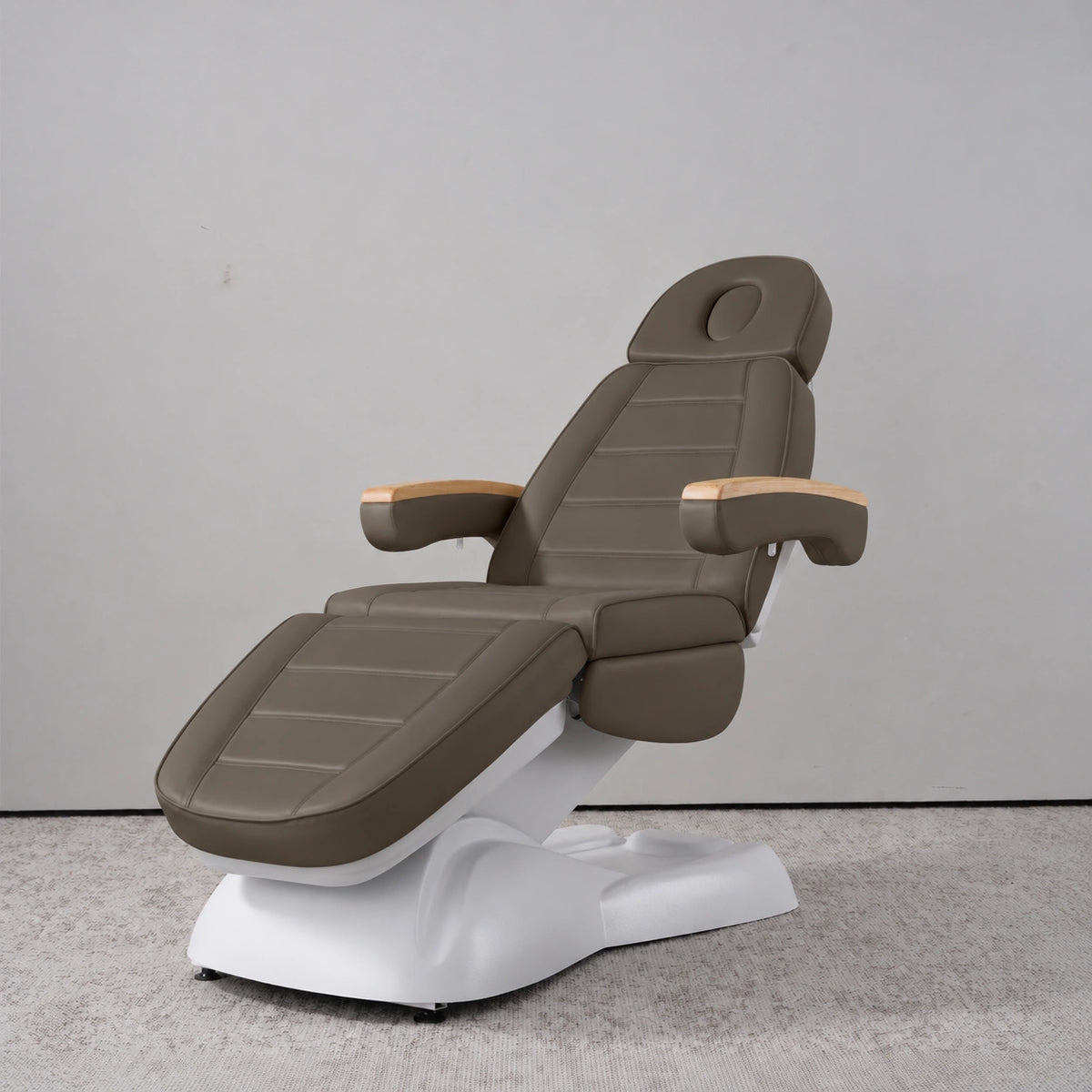 Manufakturo Grace Cocoa Mocha electric beauty bed in a treatment position, with wooden armrest caps and a white sculpted base.