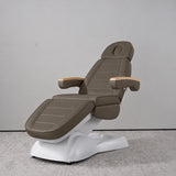 Manufakturo Grace Cocoa Mocha electric beauty bed in a treatment position, with wooden armrest caps and a white sculpted base.