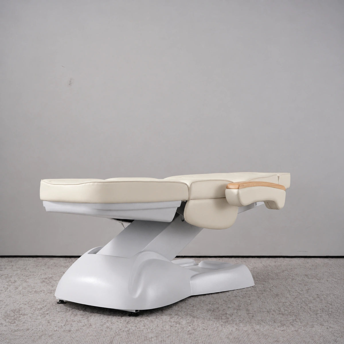 Manufakturo Grace Creamy electric beauty bed lying flat, with wooden armrest caps and the original white inclined lift and sculpted base.