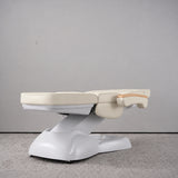 Manufakturo Grace Creamy electric beauty bed lying flat, with wooden armrest caps and the original white inclined lift and sculpted base.