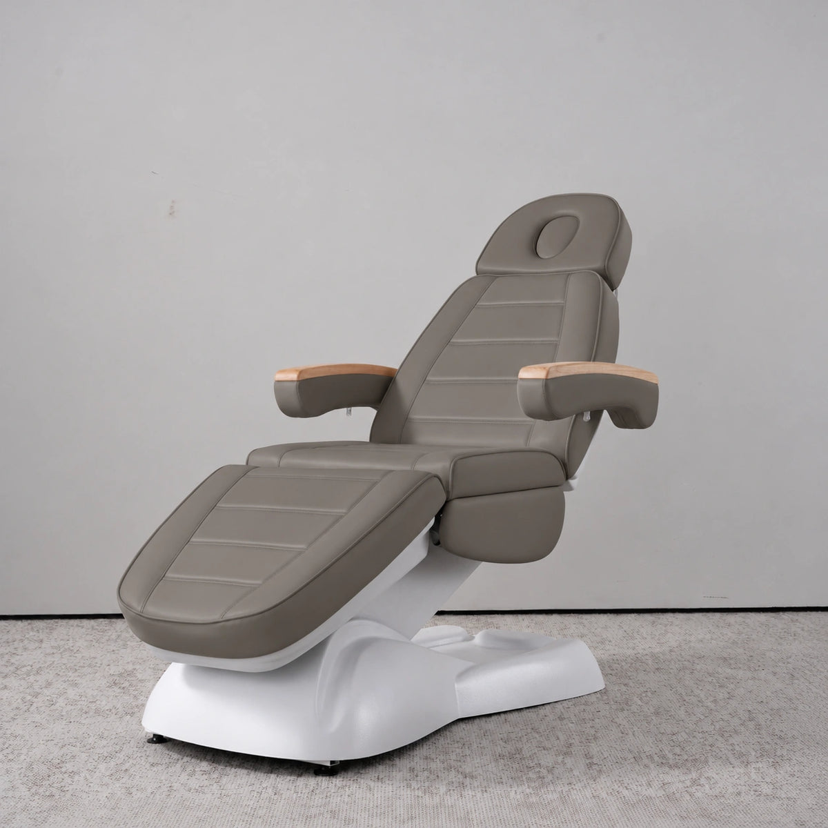 Manufakturo Grace Deep Ash electric beauty bed in a treatment position, with wooden armrest caps and a white sculpted base.