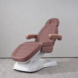 Manufakturo Grace Dusty Rose electric beauty bed in a treatment position, with wooden armrest caps and a white sculpted base.