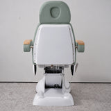 Rear view of the Manufakturo Grace Olive electric beauty bed, showing the upholstered headrest, white rigid rear cover and adjustment mechanism.