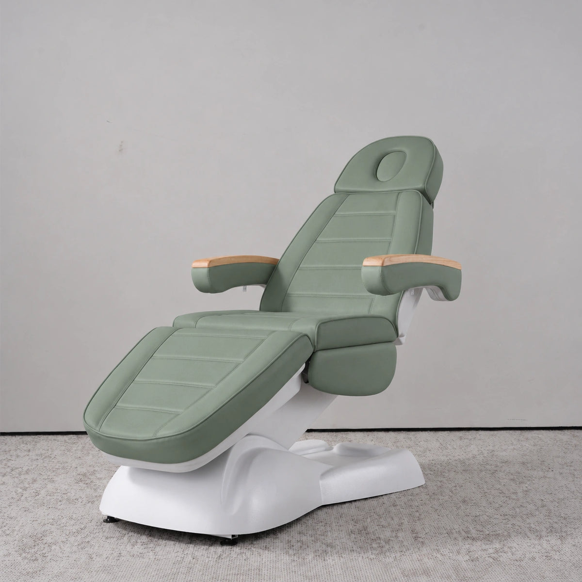 Manufakturo Grace Olive electric beauty bed in a treatment position, with wooden armrest caps and a white sculpted base.