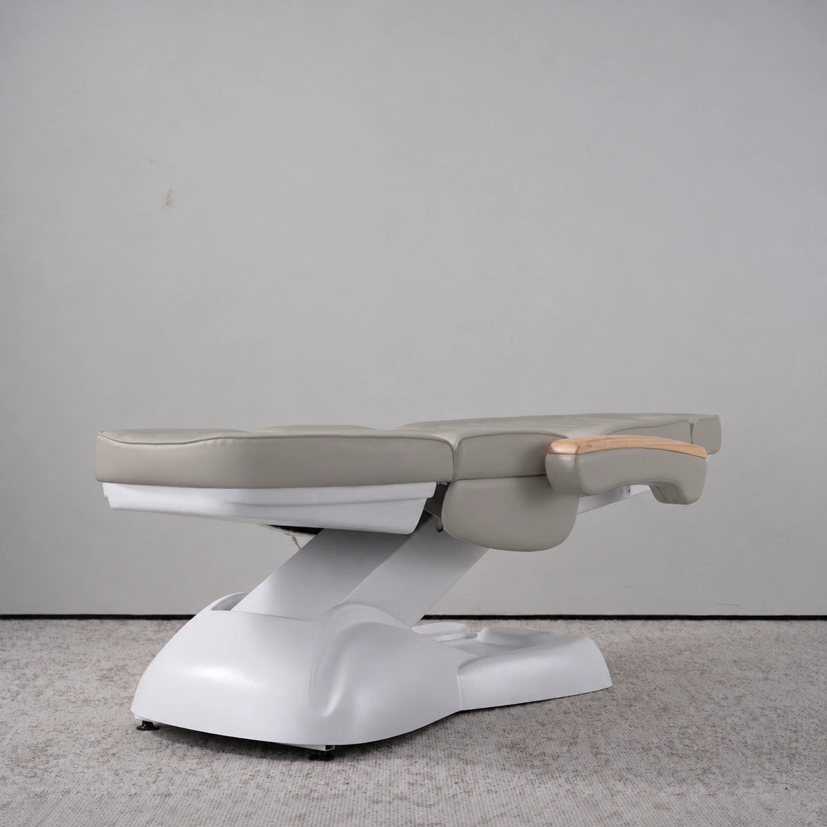 Manufakturo Grace Pearl Greige electric beauty bed lying flat, with wooden armrest caps and the original white inclined lift and sculpted base.
