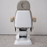 Rear view of the Manufakturo Grace Pearl Greige electric beauty bed, showing the upholstered headrest, white rigid rear cover and adjustment mechanism.