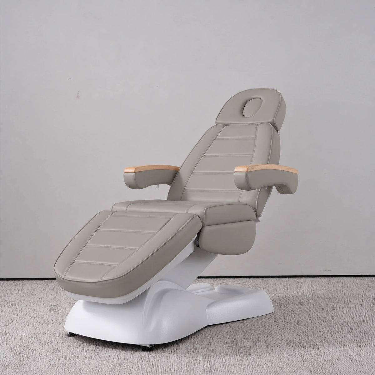 Manufakturo Grace Pearl Greige electric beauty bed in a treatment position, with wooden armrest caps and a white sculpted base.