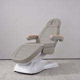 Manufakturo Grace Pearl Greige electric beauty bed in a treatment position, with wooden armrest caps and a white sculpted base.
