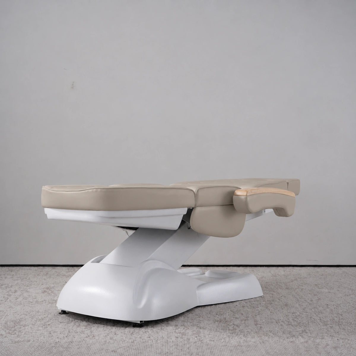 Manufakturo Grace Stone Taupe electric beauty bed lying flat, with wooden armrest caps and the original white inclined lift and sculpted base.