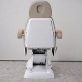 Rear view of the Manufakturo Grace Stone Taupe electric beauty bed, showing the upholstered headrest, white rigid rear cover and adjustment mechanism.
