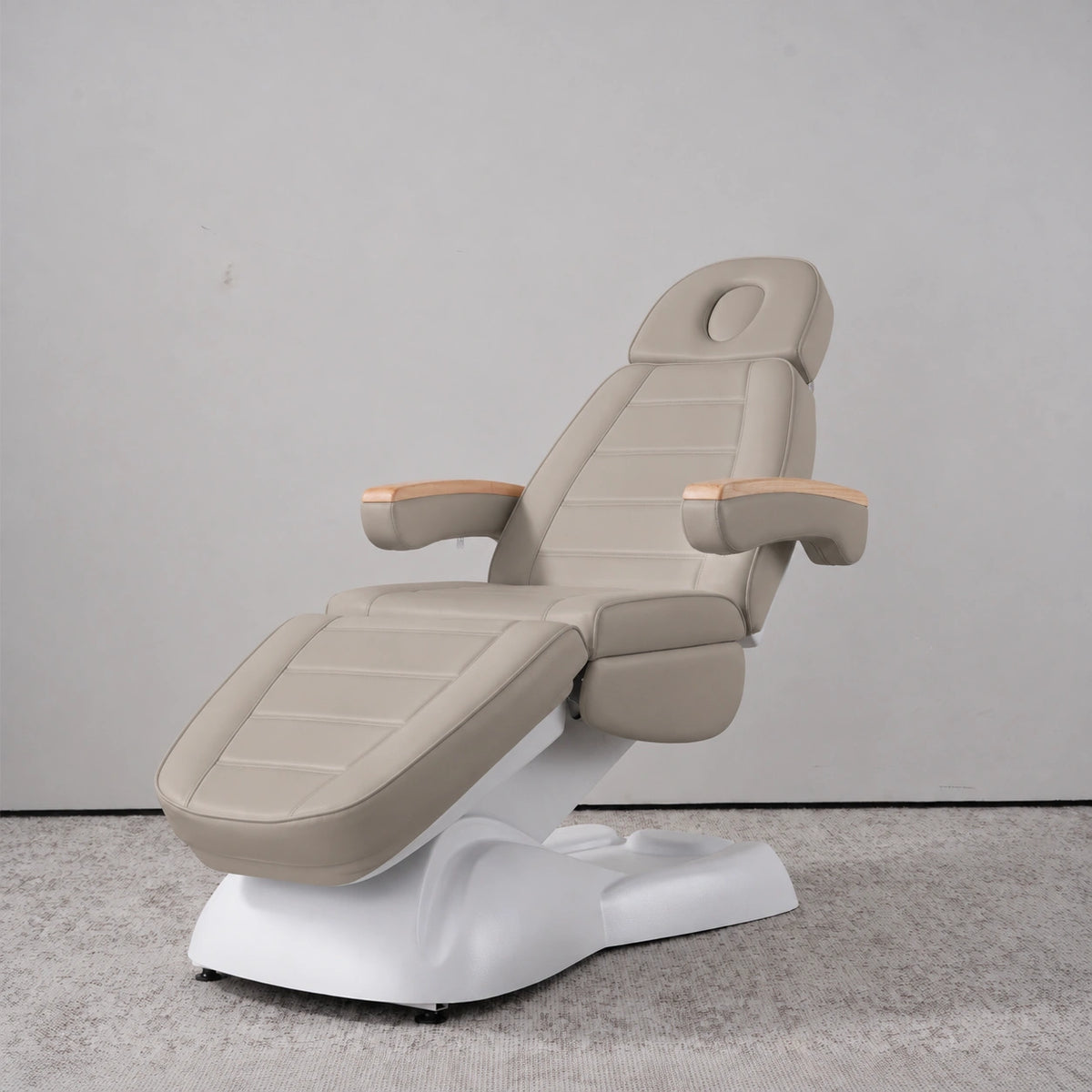 Manufakturo Grace Stone Taupe electric beauty bed in a treatment position, with wooden armrest caps and a white sculpted base.