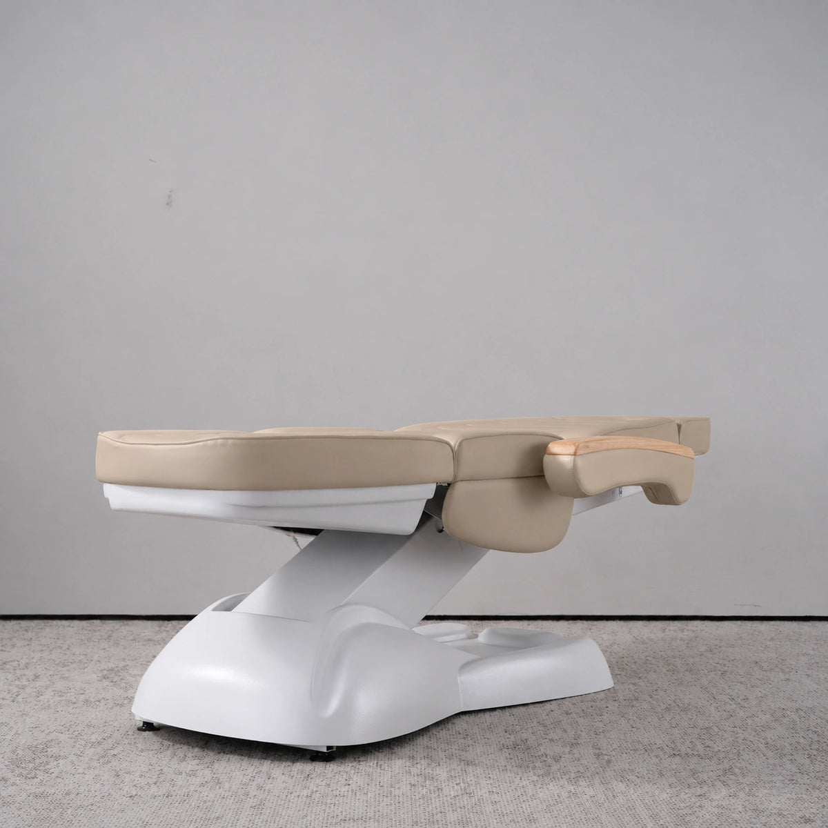 Manufakturo Grace Warm Beige electric beauty bed lying flat, with wooden armrest caps and the original white inclined lift and sculpted base.