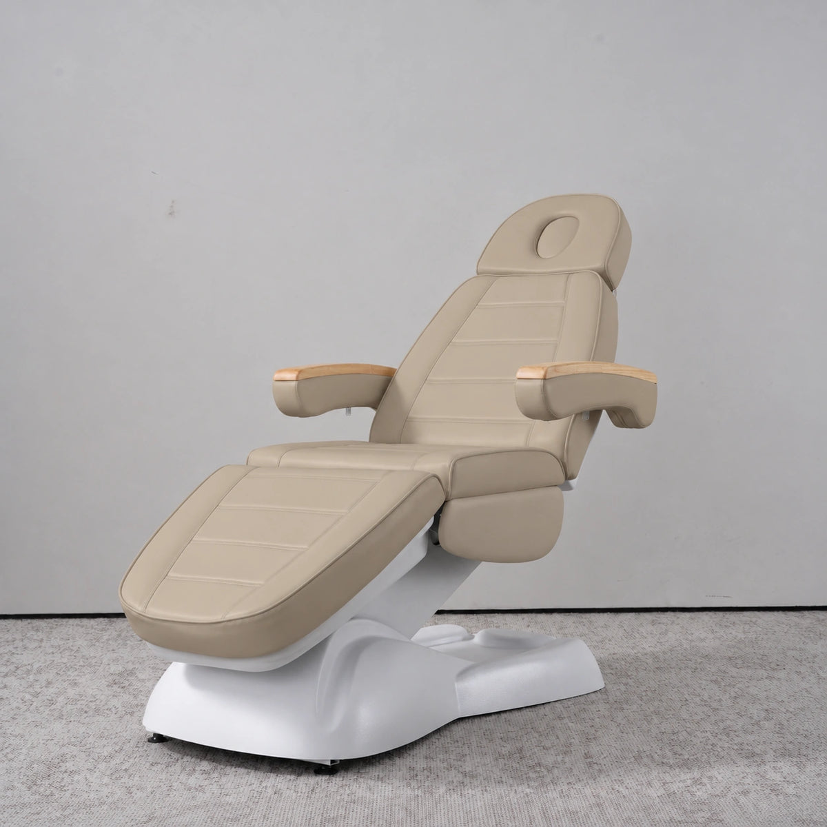 Manufakturo Grace Warm Beige electric beauty bed in a treatment position, with wooden armrest caps and a white sculpted base.