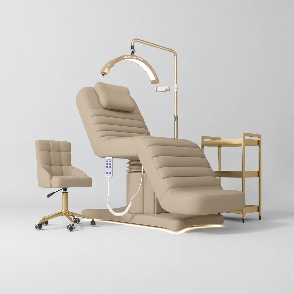 Manufakturo Grandeur Warm Beige complete studio set with beauty bed, Noblesse chair, gold trolley and V3 Pro Gold treatment lamp, photographed against the original grey studio background.