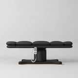 Manufakturo Imperial Signature heated electric beauty bed in Black, shown fully flat from the side with matching base and white remote control.