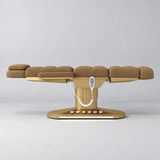 Manufakturo Orielle A Brown teddy electric beauty bed in a flat position viewed from the side, with gold oval base and hand-held controller.