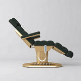 Manufakturo Orielle A Dark Green teddy electric beauty bed shown from the side in a treatment position, with gold oval base and hand-held controller.