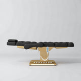 Manufakturo Orielle B Black electric beauty bed in a flat position viewed from the side, with gold base and hand-held controller.