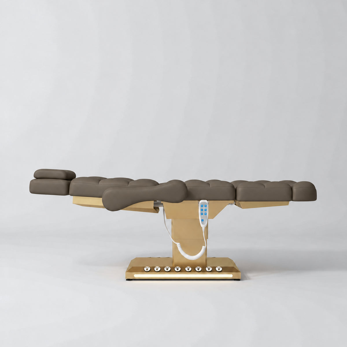Manufakturo Orielle B Cocoa Mocha electric beauty bed in a flat position viewed from the side, with gold base and hand-held controller.