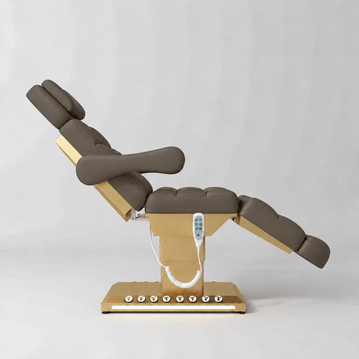 Manufakturo Orielle B Cocoa Mocha electric beauty bed shown from the side in a treatment position, with gold base and hand-held controller.