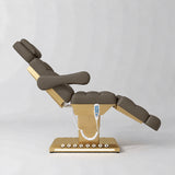 Manufakturo Orielle B Cocoa Mocha electric beauty bed shown from the side in a treatment position, with gold base and hand-held controller.