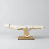 Manufakturo Orielle B Creamy electric beauty bed in a flat position viewed from the side, with gold base and hand-held controller.