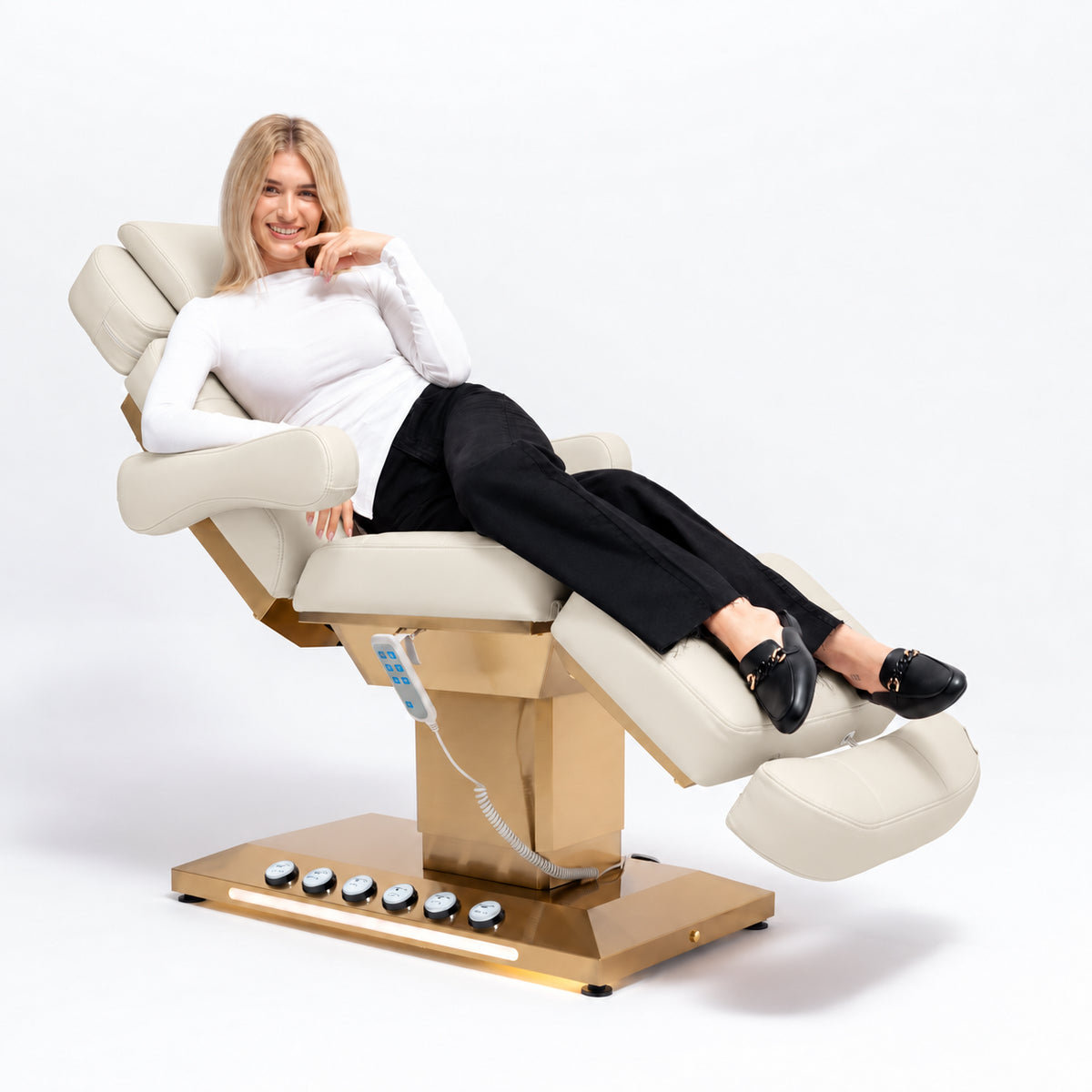 Manufakturo Orielle B Creamy beauty bed in use, showing upholstered armrests, extendable footrest, hand and foot controls and LED base lighting.