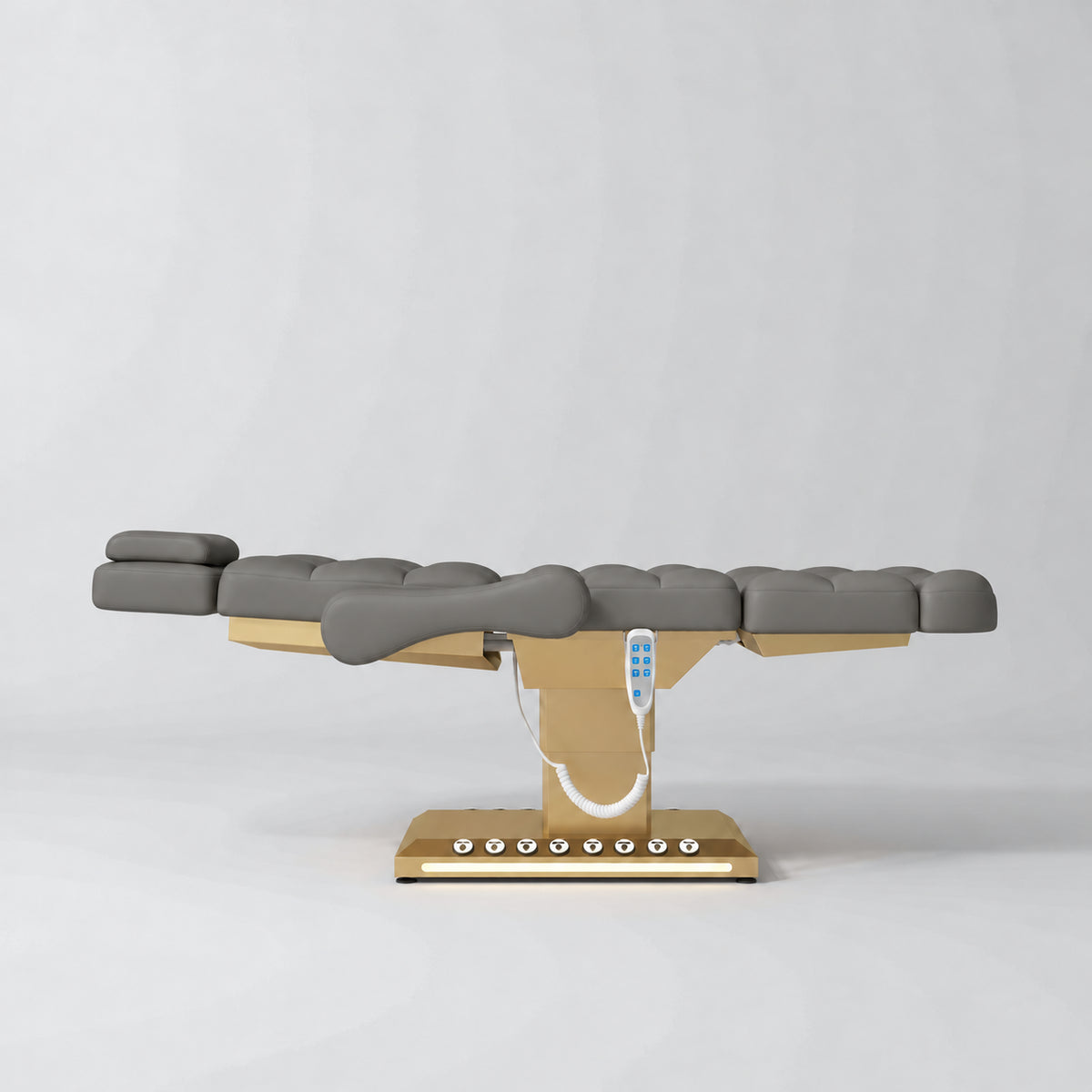 Manufakturo Orielle B Deep Ash electric beauty bed in a flat position viewed from the side, with gold base and hand-held controller.