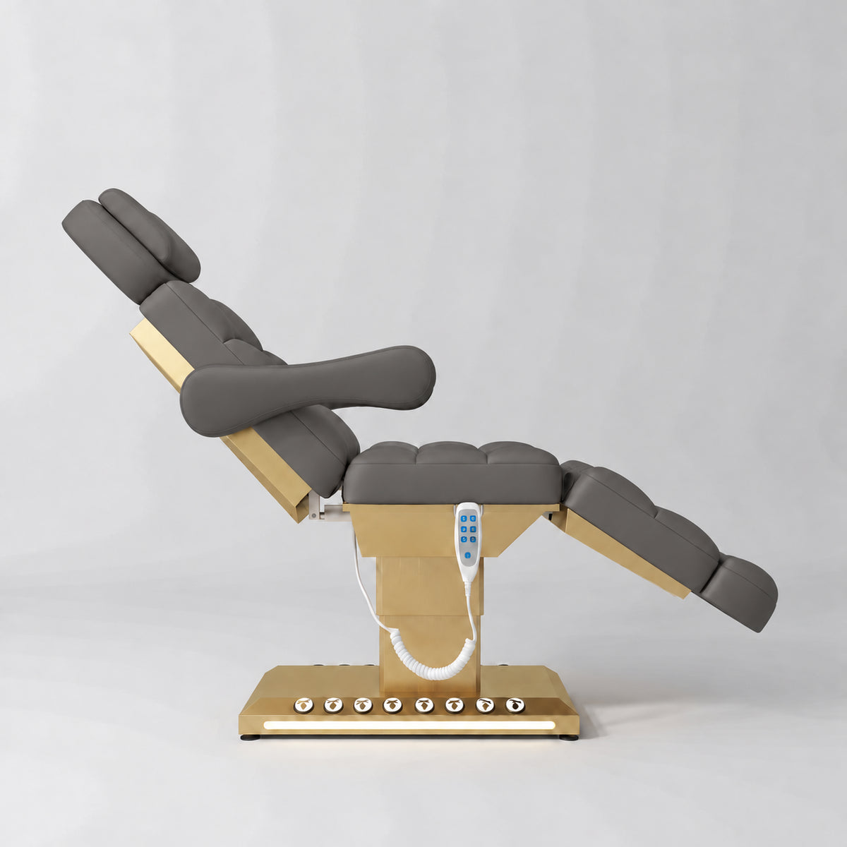 Manufakturo Orielle B Deep Ash electric beauty bed shown from the side in a treatment position, with gold base and hand-held controller.