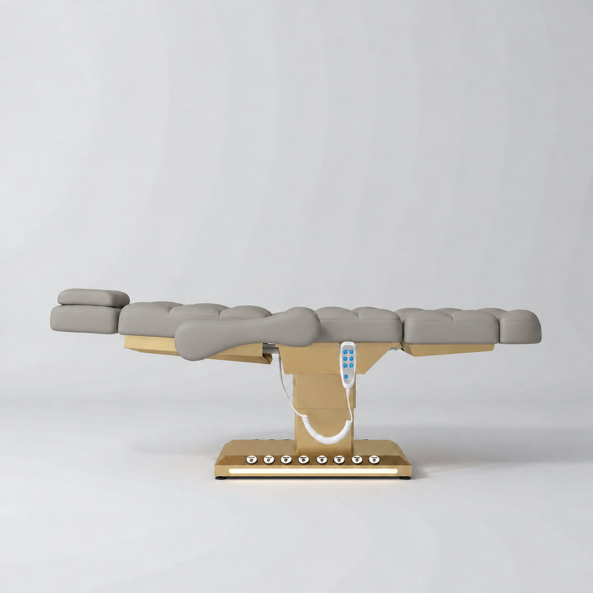 Manufakturo Orielle B Pearl Greige electric beauty bed in a flat position viewed from the side, with gold base and hand-held controller.