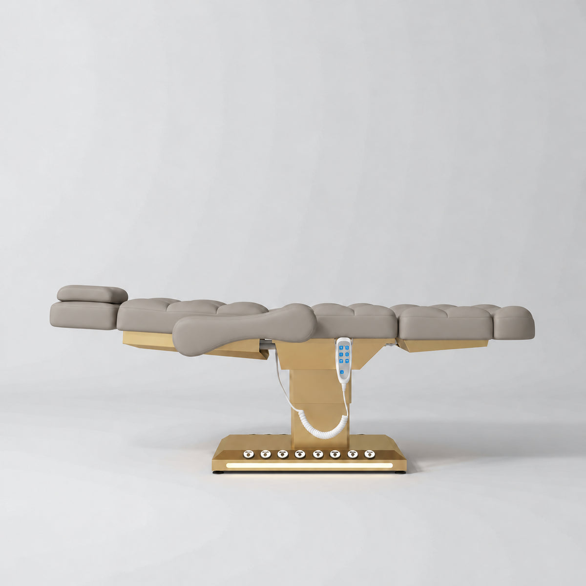 Manufakturo Orielle B Stone Taupe electric beauty bed in a flat position viewed from the side, with gold base and hand-held controller.