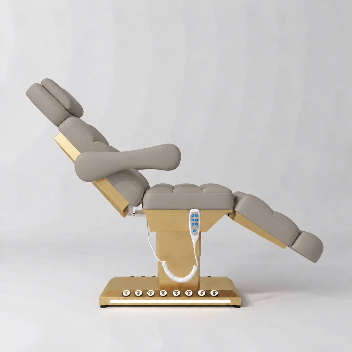 Manufakturo Orielle B Stone Taupe electric beauty bed shown from the side in a treatment position, with gold base and hand-held controller.