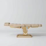 Manufakturo Orielle B Warm Beige electric beauty bed in a flat position viewed from the side, with gold base and hand-held controller.