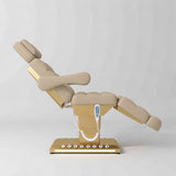 Manufakturo Orielle B Warm Beige electric beauty bed shown from the side in a treatment position, with gold base and hand-held controller.