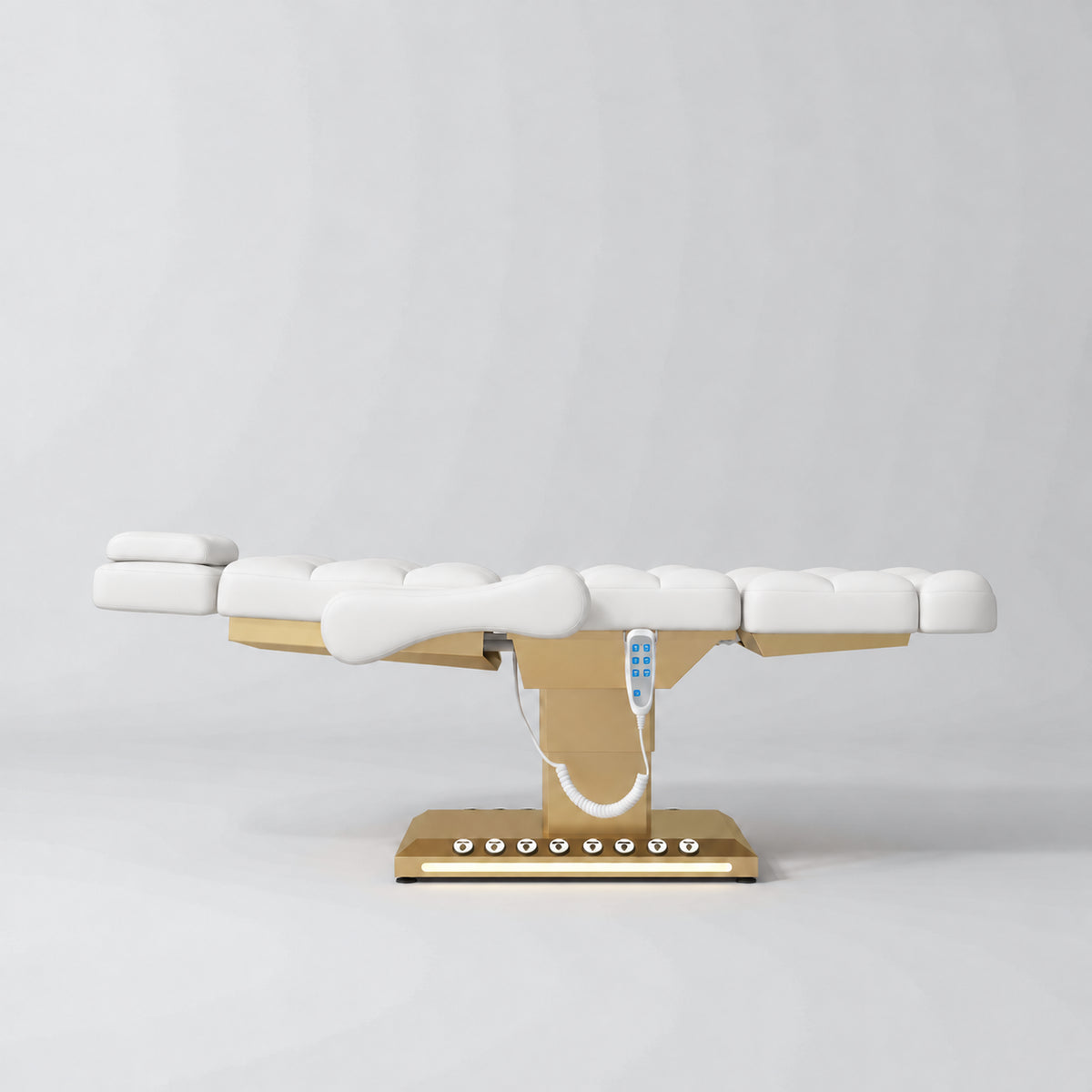 Manufakturo Orielle B White electric beauty bed in a flat position viewed from the side, with gold base and hand-held controller.