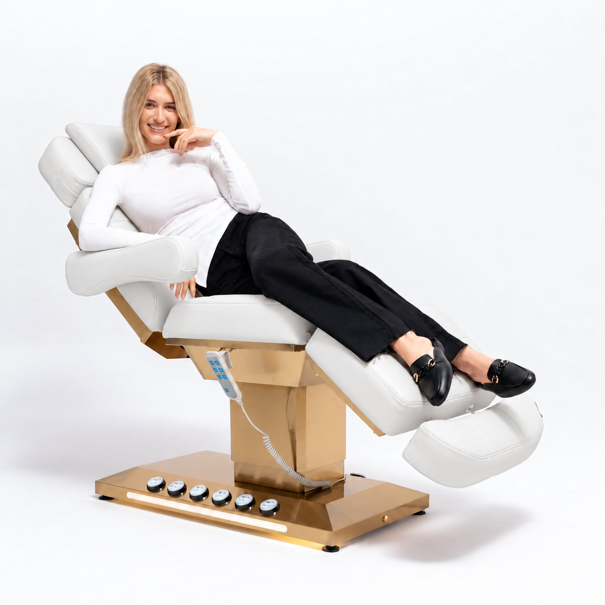 Manufakturo Orielle B White beauty bed in use, showing upholstered armrests, extendable footrest, hand and foot controls and LED base lighting.